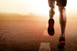 Close-up of a runner's legs and shoes as they run on an open road, with a warm, golden sunrise in the background.